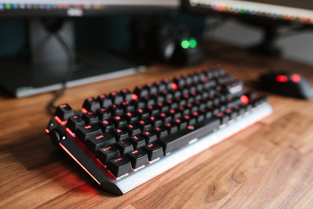 Contemporary computer backlit keyboard placed on wooden desk near mouse in light room